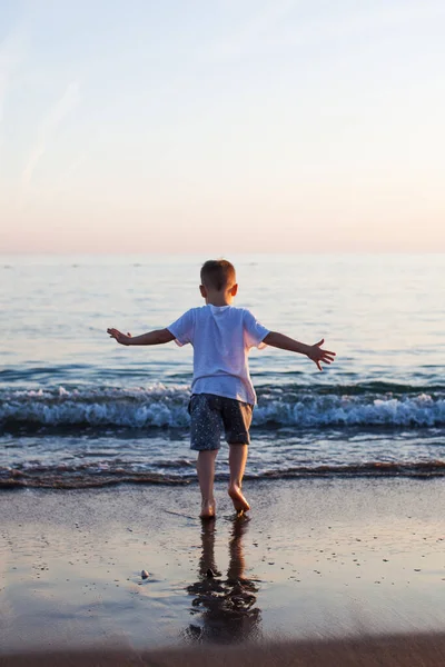 A little boy runs along a sandy beach in the sea at sunset. — Stock Photo, Image