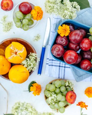 Birçok meyve-üzüm, erik, mandalina. Açık arkaplan, bir sürü renk ve bir mutfak havlusu..
