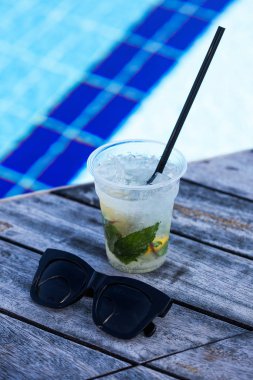 Açık havuzun arka planında pipetli ve siyah güneş gözlüklü bir bardakta mojito kokteyli. Otel her şeyi kapsıyor..
