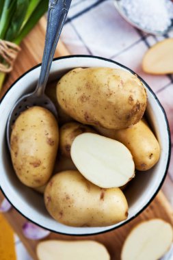 Tahta bir kaşık ile metal bir tabakta yıkanmış çiğ patateslerin nefis bir fotoğrafı, yeşil soğanların arka planında, büyük tuz. Patatesler boydan boya kesilmiş..