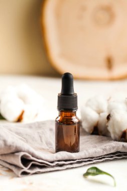 Pamuk çiçeklerinin etrafındaki gri bir peçete üzerinde yüz ve vücut derisi için serum yağı. Kozmetik.