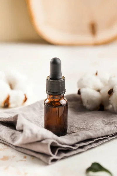 Pamuk çiçeklerinin etrafındaki gri bir peçete üzerinde yüz ve vücut derisi için serum yağı. Kozmetik.