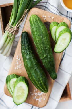 Uzun olgun salatalıklar ve büyük bir tuz ve bir demet yeşil soğanla ahşap bir tahtada kesilmiş. Yemek fotoğrafı..