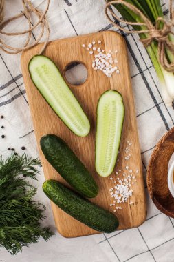 Olgun salatalıklar bir bütün ve büyük bir tuz ve bir demet yeşil soğanla ahşap bir tahtada kesilmiş. Yemek fotoğrafı..