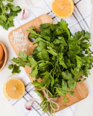 Kaba tuz, sarımsak karanfili ve limon dilimleriyle çevrili tahta bir tahtanın üzerinde bir demet taze maydanoz. Yemek fotoğrafı..