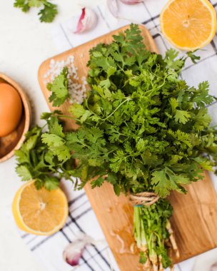 Kaba tuz, sarımsak ve limon dilimleriyle çevrili ahşap bir tahtanın üzerinde bir demet taze kişniş otu.. 