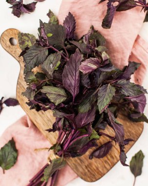 Ahşap bir tahtaya yakın çekimde bir demet taze mor fesleğen ve açık arkaplanda pembe bir peçete..