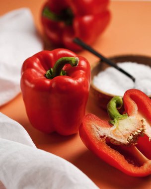 Olgun kırmızı biber bütün ve kesikte, beyaz tuzlu bir tabak ve beyaz bir mutfak havlusunun yanında.