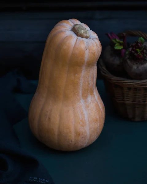 Una larga calabaza entera madura en primer plano sobre un fondo oscuro, con remolachas en una cesta de mimbre en el fondo . —  Fotos de Stock