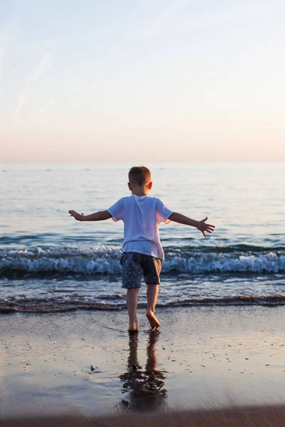 A little boy runs along a sandy beach in the sea at sunset — Stock Photo, Image