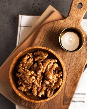 Ahşap bir arka planda ahşap bir tabakta soyulmuş bir avuç ceviz ve mumlar..