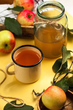 Bardakta taze sıkılmış elma suyu ve olgun kırmızı ve sarı elmalarla çevrili cam bir kavanozda..