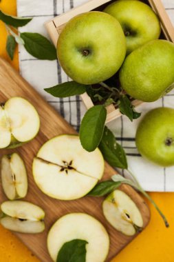 Ripe juicy green apples whole and cut on a wooden Board with green leaves on a yellow background. Country still life.