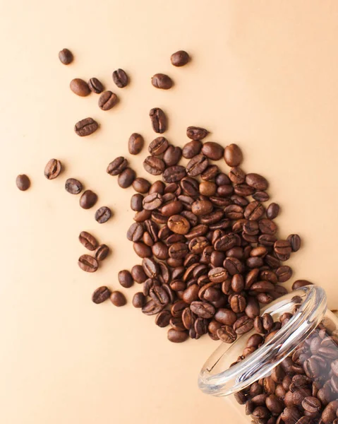 Primer plano de granos de café se derrama de un frasco de vidrio sobre un fondo marrón claro. Para cafés y cafeterías . — Foto de Stock