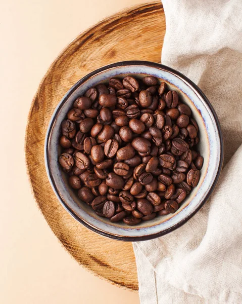 Granos de café Arabica en un tazón de cerámica en una bandeja de madera sobre un fondo marrón . — Foto de Stock