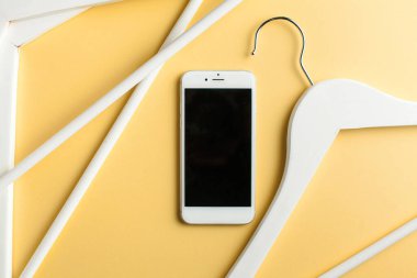  Sarı arka planda cep telefonu ve elbise askısı var. Flatlay. Boşluğu kopyala. 