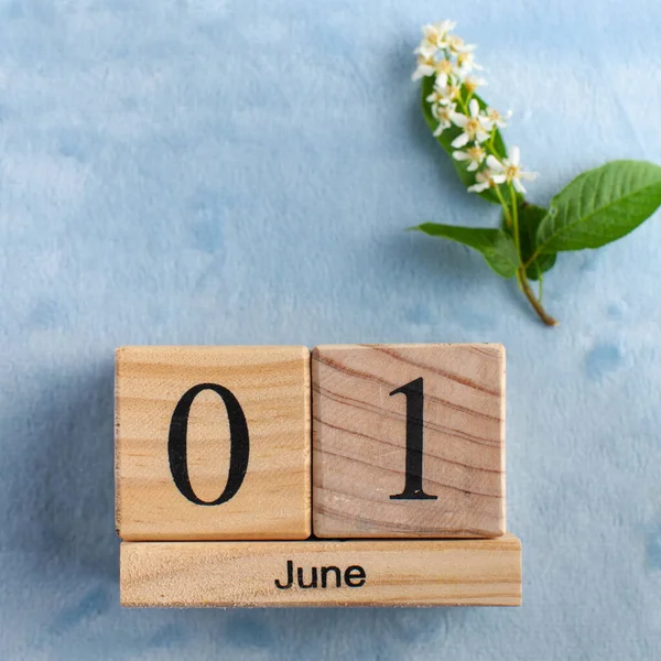 Wooden calendar June 1 on a blue background with white flowers. The concept of the beginning of summer, the first day of June, Children's Day.