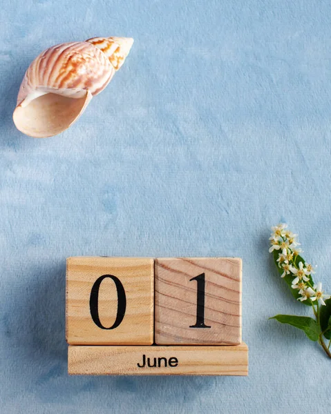 Wooden calendar June 1 on a blue background with white flowers. The concept of the beginning of summer, the first day of June, Children\'s Day.