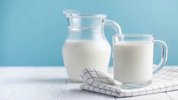  Mavi arka planda bir bardak süt ve bir sürahi süt. Çiftlik ürünleri konsepti, süt günü..