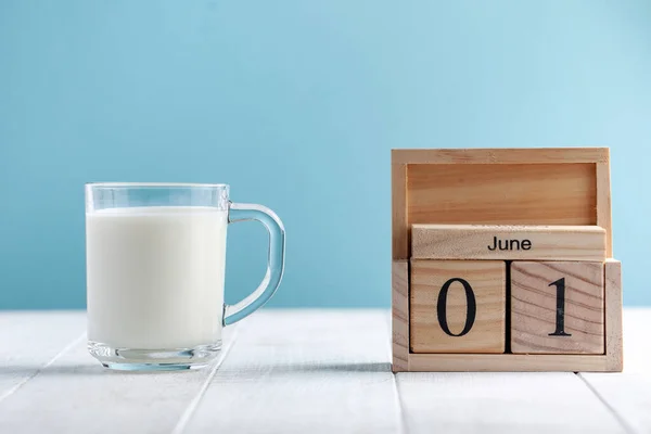 Wooden calendar June 1, a mug of milk on a blue background. The concept of Milk Day, Children\'s Day, June 1. food photo.