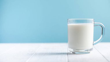 Mavi arka planda bir bardak süt. Çiftlik süt ürünleri konsepti, süt kullanımı. Uzayı kopyala Yatay yemek fotoğrafı..
