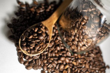 Hafif arka planda cam kavanozlu, tahta kaşıkta kahve çekirdekleri.