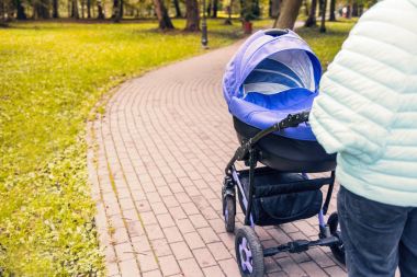 Bir bebek arabası yeşil ağaçlar arka planı parkta elini kolunu sallaya dönüyor. tonda fotoğraf