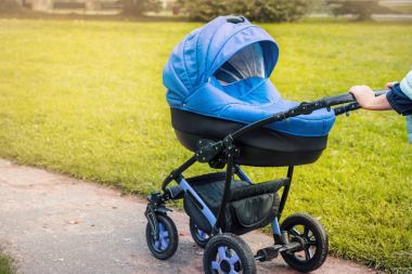 Bir bebek arabası yeşil ağaçlar arka planı parkta elini kolunu sallaya dönüyor. tonda fotoğraf