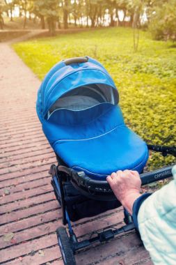 Bir bebek arabası yeşil ağaçlar arka planı parkta elini kolunu sallaya dönüyor. tonda fotoğraf