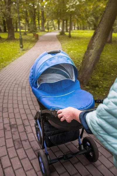 Bir bebek arabası yeşil ağaçlar arka planı parkta elini kolunu sallaya dönüyor. tonda fotoğraf