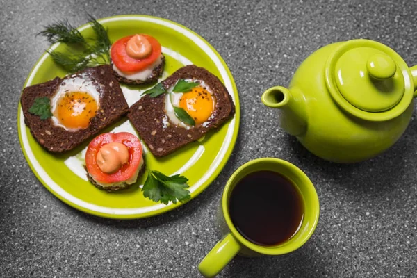 Breakfast -  toast with processed cheese tomato, fried eggs , fried eggs, teapot and cup of tea on a gray  background. Flat lay. Top view.