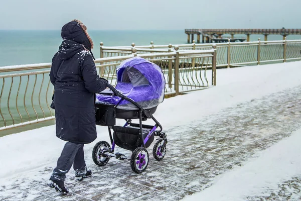 Madre feliz con cochecito de bebé caminando cerca de la orilla del mar y E — Foto de Stock
