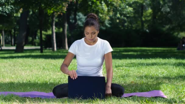 Yoga féminin dans le parc travaillant sur un ordinateur portable — Video