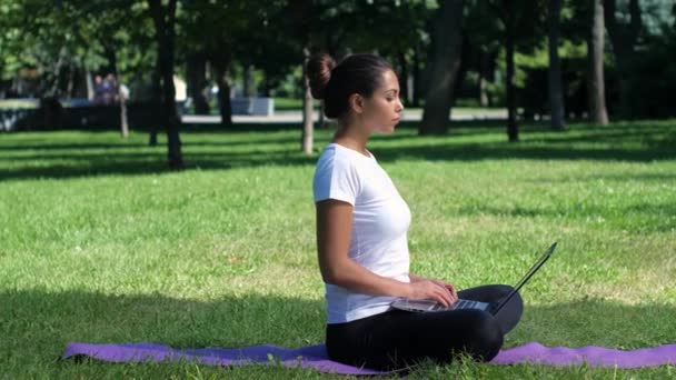 Yoga féminin dans le parc travaillant sur un ordinateur portable — Video