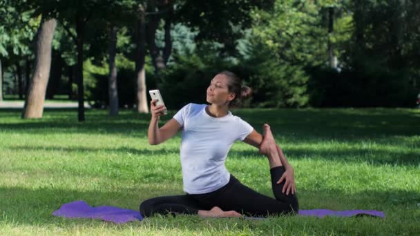 Tjejen sitter på en matta och göra selfie med smart telefon i yoga position — Stockvideo