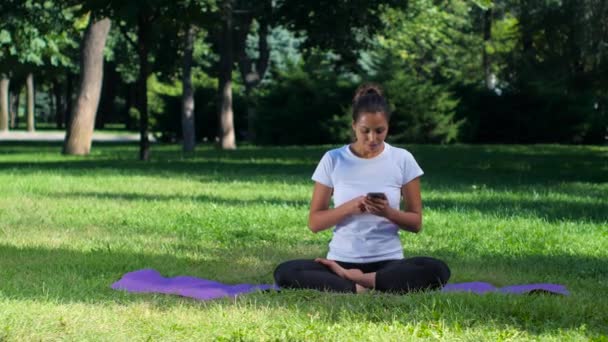 Menina fazendo ioga no parque e falando no celular — Vídeo de Stock