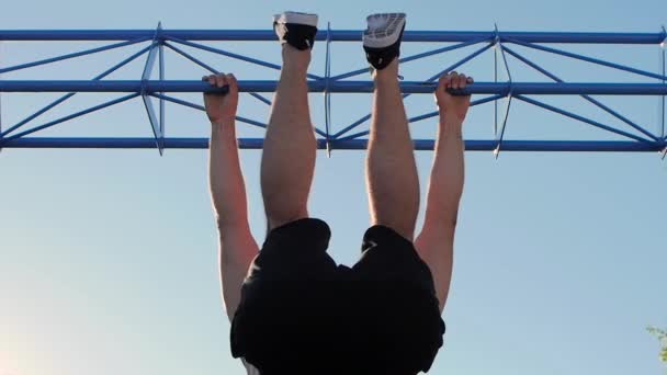 El hombre levanta sus piernas a la barra horizontal. Movimiento lento — Vídeos de Stock