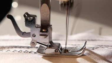 Dikiş makinesi beyaz kumaş üzerine bir zikzak dikiş diker. Ağır çekim