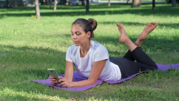 Fille se trouve sur le tapis de sport et parler sur téléphone portable — Video