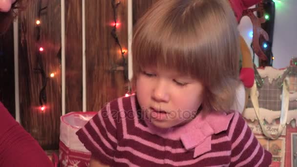 Gelukkig klein meisje zit in de buurt van een kerstboom ingericht, houten achtergrond — Stockvideo