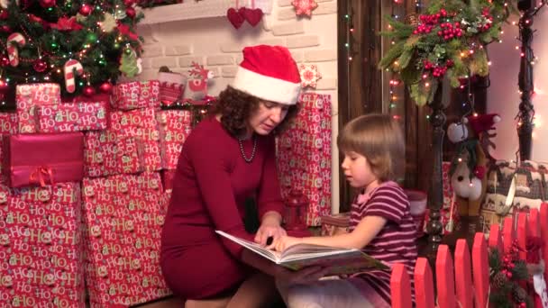 Ung mamma och hennes lilla dotter med julklappar läser boken av en jul — Stockvideo