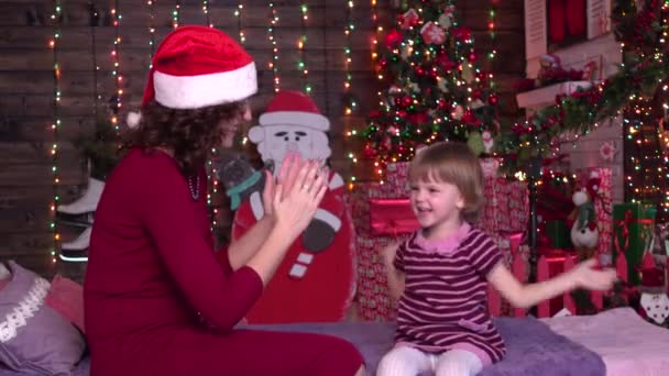 Jonge dochter en moeder zitten samen op een bed, klappen hun handen, Christmas decor, thuis, familie — Stockvideo