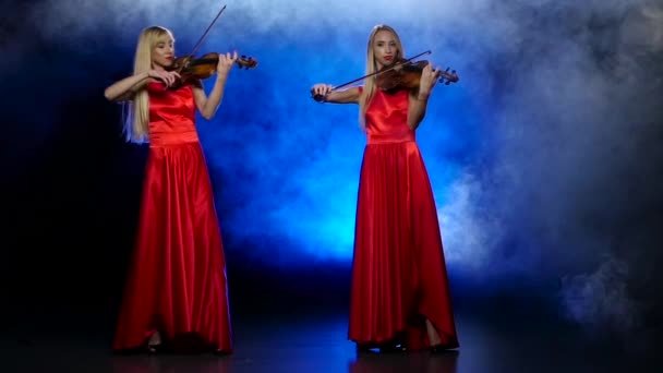 Duas meninas loira para tocar violino. Fundo fumegante com luz de fundo. Movimento lento — Vídeo de Stock