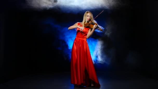 Дівчина в червоній сукні грає на скрипці. Студія. Дим — стокове відео