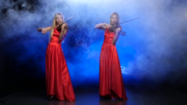 Две девушки в красном платье играют на скрипке. Студия. Дым — стоковое видео