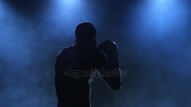 Boksör mücadele öncesi egzersiz gösterir. Siluet koyu arka plan üzerinde