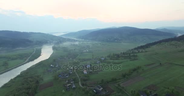 Село на горбистій місцевості на березі річки — стокове відео