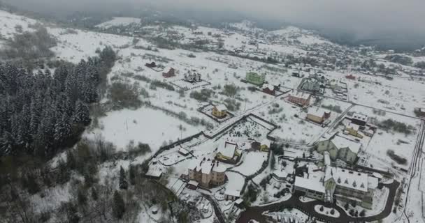 Zimní svahy kopce poseté sněhem. Zasněžená vesnice. Letecký pohled — Stock video