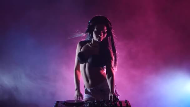 Girl DJ gira um estande de DJ, atrás de suas luzes multicoloridas e fumaça. Silhueta — Vídeo de Stock
