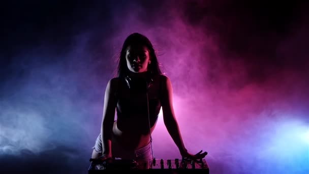 Chica DJ jugando en los tocadiscos, detrás de sus luces azules rosadas. Movimiento lento — Vídeos de Stock